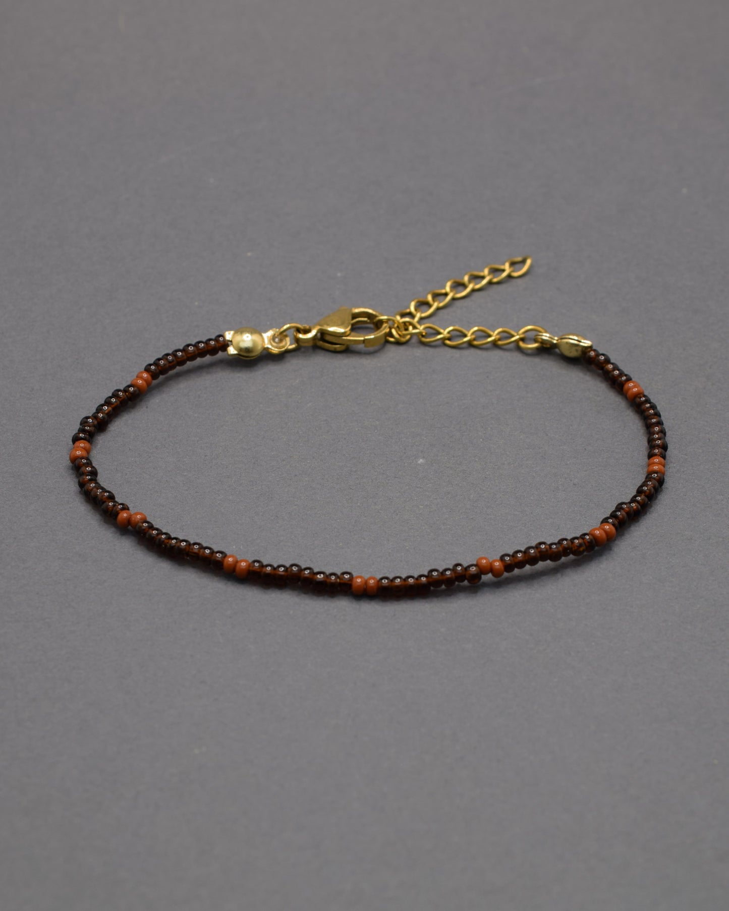 Pulseira de missangas castanhas semitransparentes com padrão castanho opaco. Elegante e versátil, ideal para um look natural e sofisticado.