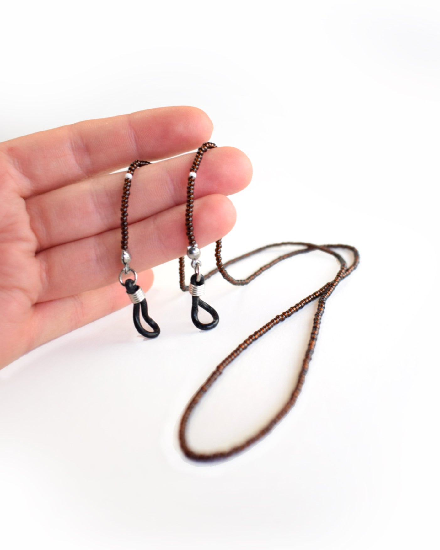 Acessórios de moda online - Nesta corrente de óculos a cor castanha escura das missangas transparentes quando refletida com a luz, retorna um bordô muito característico do tão apreciado suco das uvas fermentado e rotulado com o ano da sua colheita, representado por missangas de vidro brancas, um requinte de bijuteria.