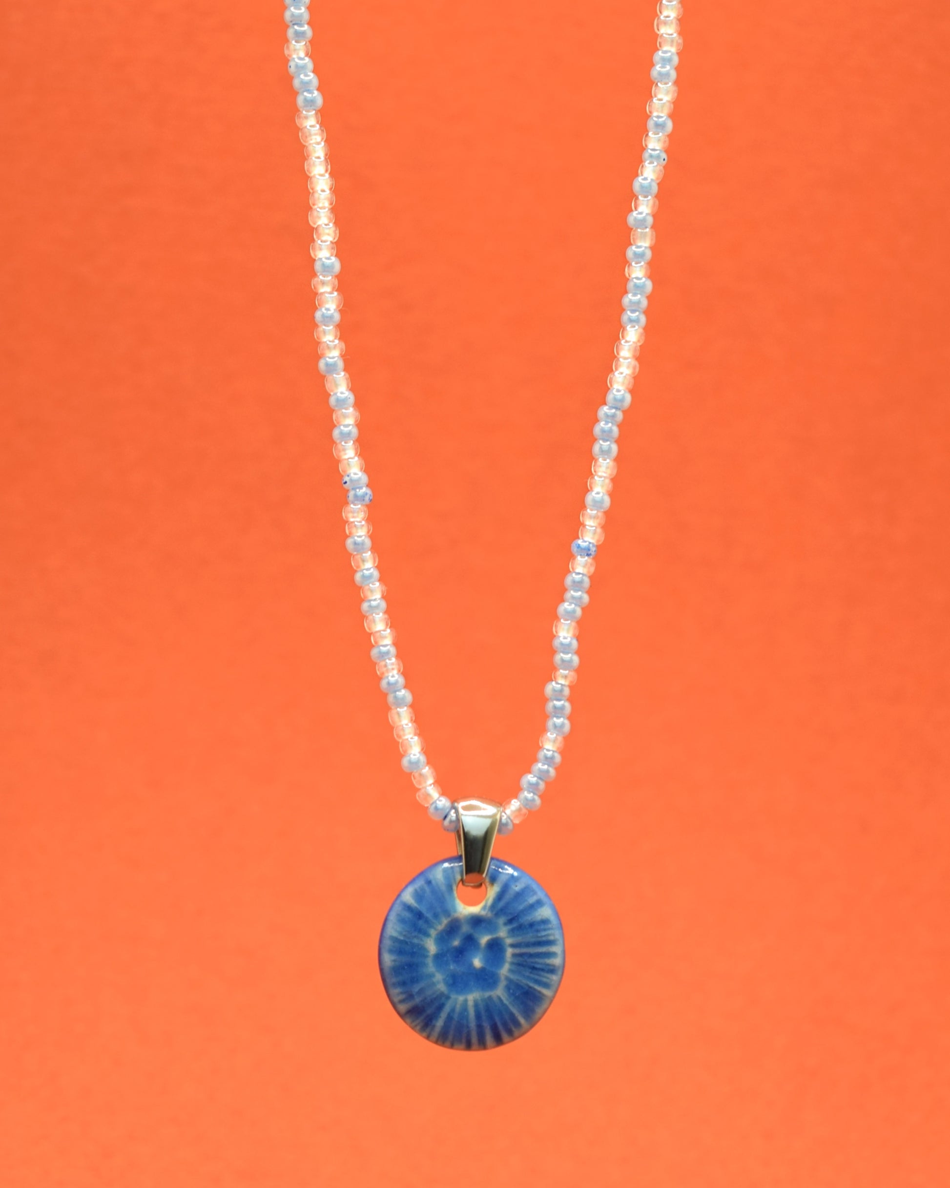 Colar cativante com missangas de vidro em uma mistura suave de tons azul claro, complementado por um elegante pendente de cerâmica azul, inspirado numa delicada flor do mar. Uma fusão encantadora de cores que adiciona um toque único e sofisticado ao seu estilo.