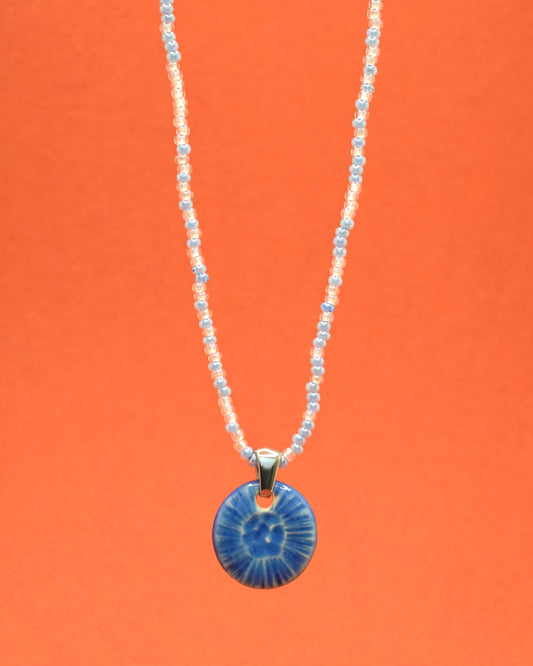 Colar cativante com missangas de vidro em uma mistura suave de tons azul claro, complementado por um elegante pendente de cerâmica azul, inspirado numa delicada flor do mar. Uma fusão encantadora de cores que adiciona um toque único e sofisticado ao seu estilo.