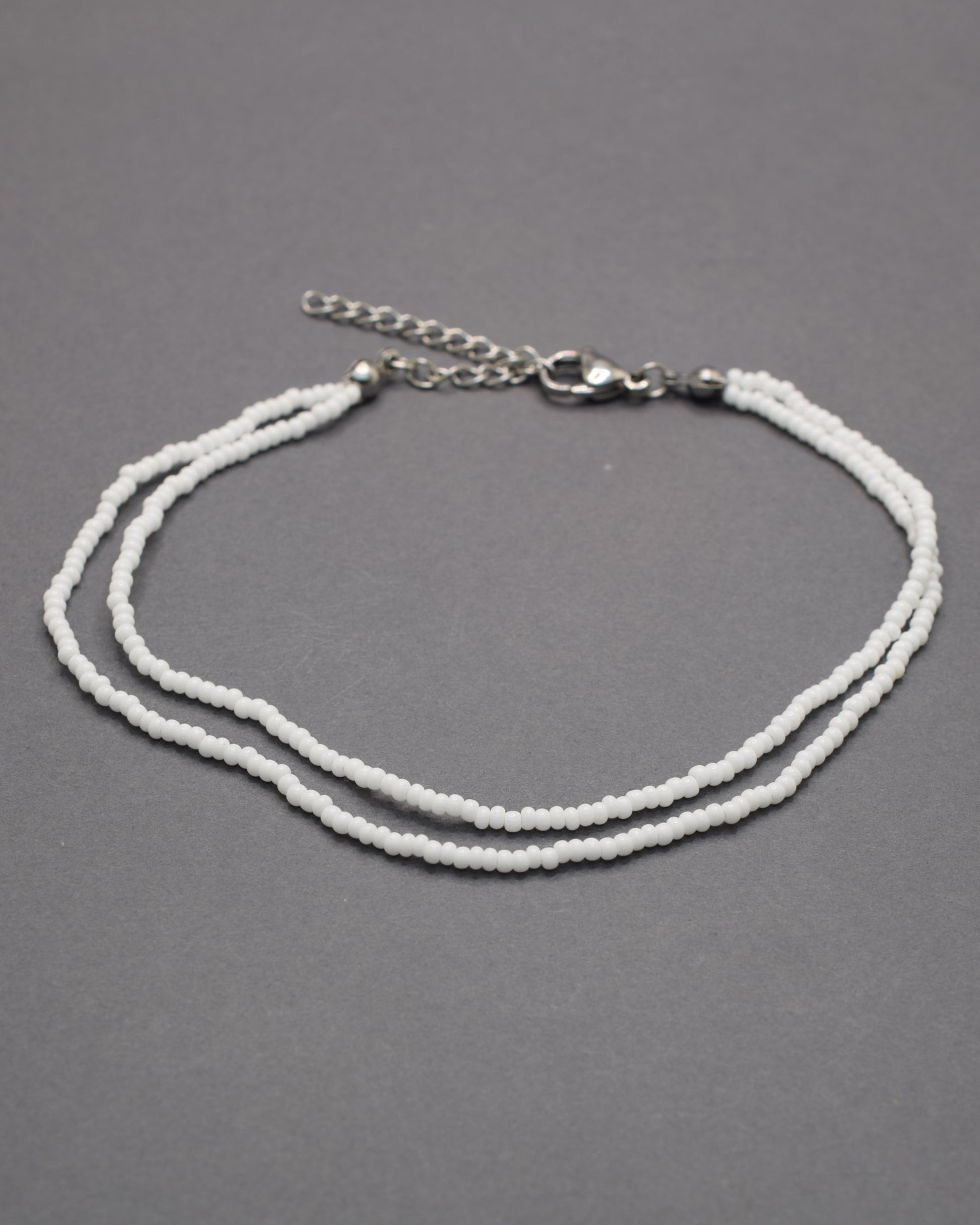 Pulseira dupla de tornozelo em missangas brancas, delicada e luminosa, perfeita para um look fresco, elegante e versátil em qualquer ocasião.