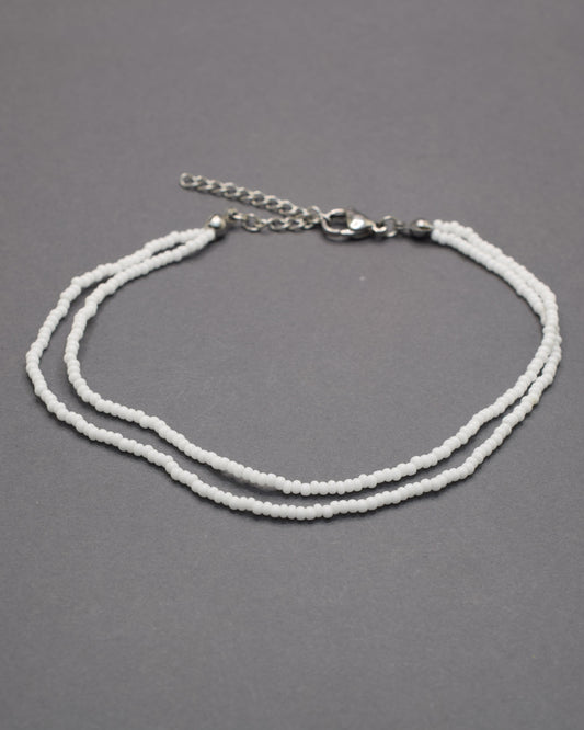 Pulseira dupla de tornozelo em missangas brancas, delicada e luminosa, perfeita para um look fresco, elegante e versátil em qualquer ocasião.