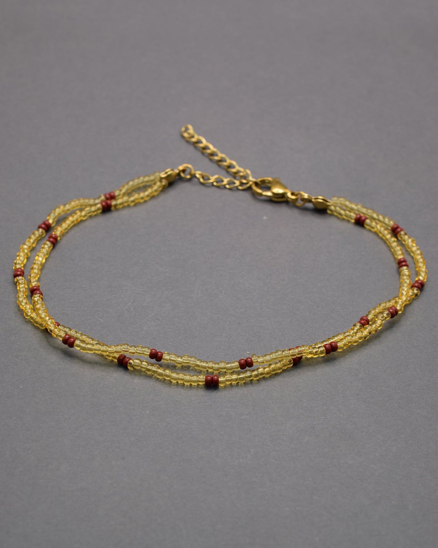 Pulseira dupla de tornozelo em missangas douradas semitransparentes com padrão bordô, elegante e sofisticada, perfeita para um toque quente e distinto.