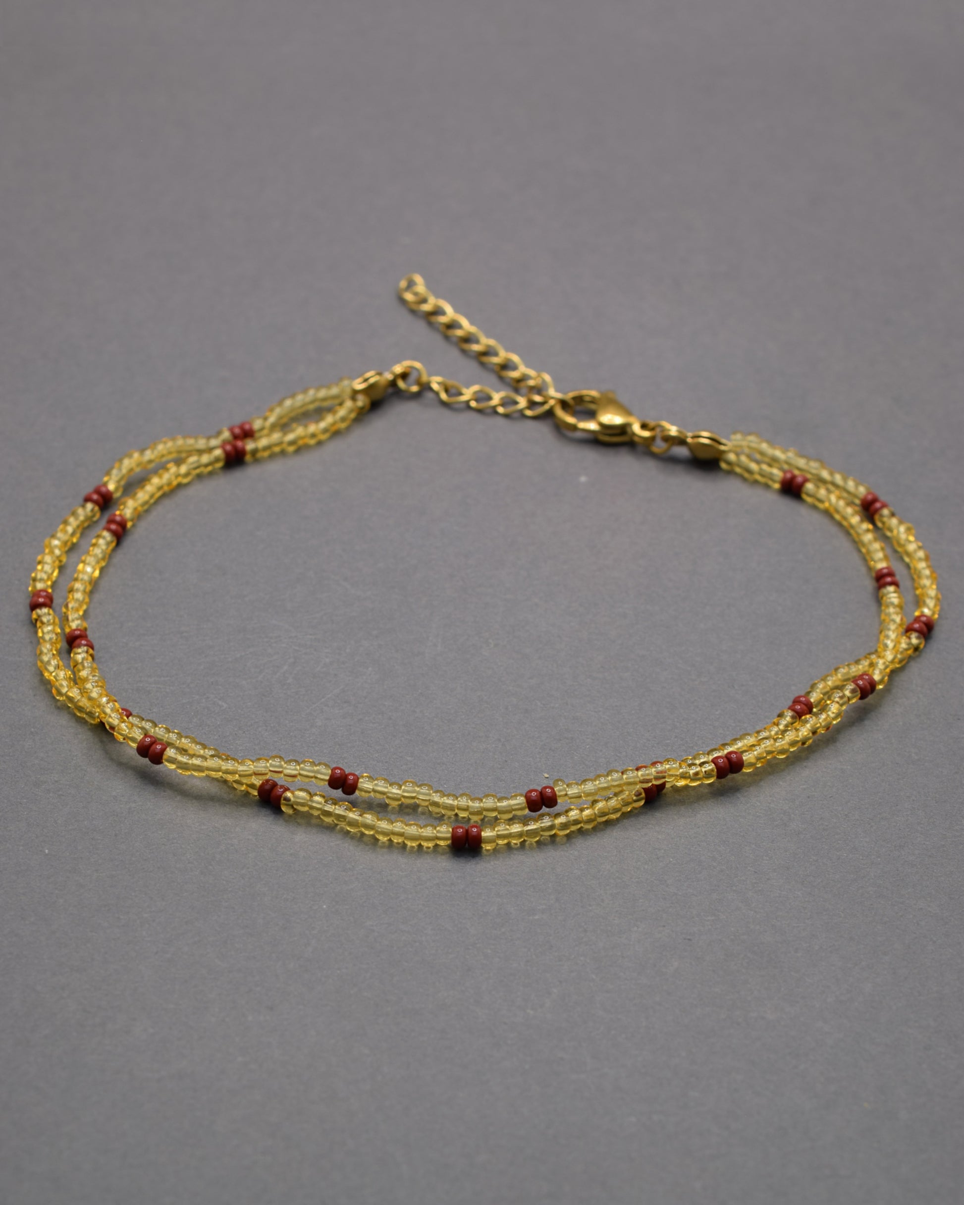 Pulseira dupla de tornozelo em missangas douradas semitransparentes com padrão bordô, elegante e sofisticada, perfeita para um toque quente e distinto.