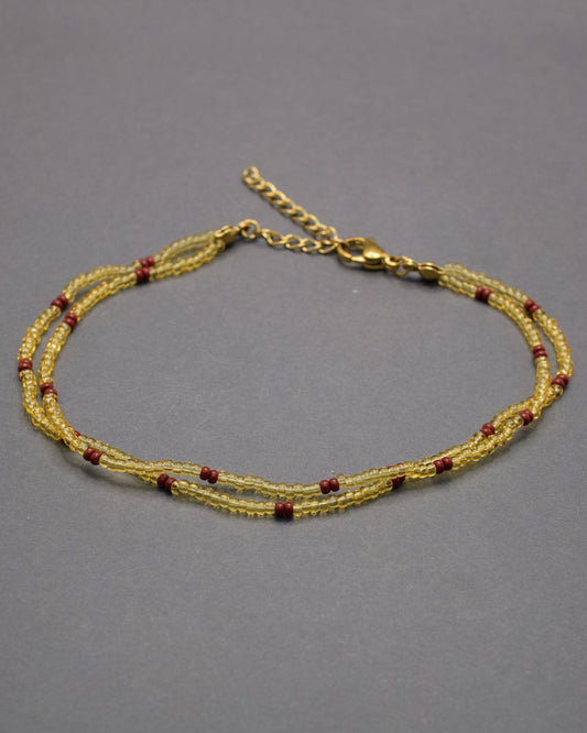 Pulseira dupla de tornozelo em missangas douradas semitransparentes com padrão bordô, elegante e sofisticada, perfeita para um toque quente e distinto.
