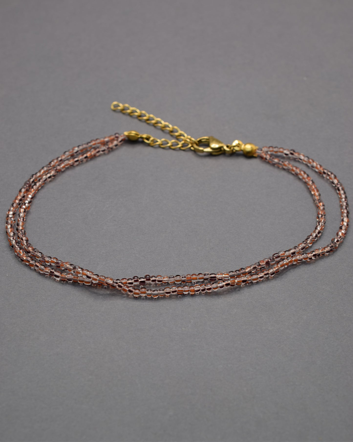 Pulseira dupla de tornozelo com missangas listradas castanhas, elegante e versátil, ideal para um toque natural e sofisticado.