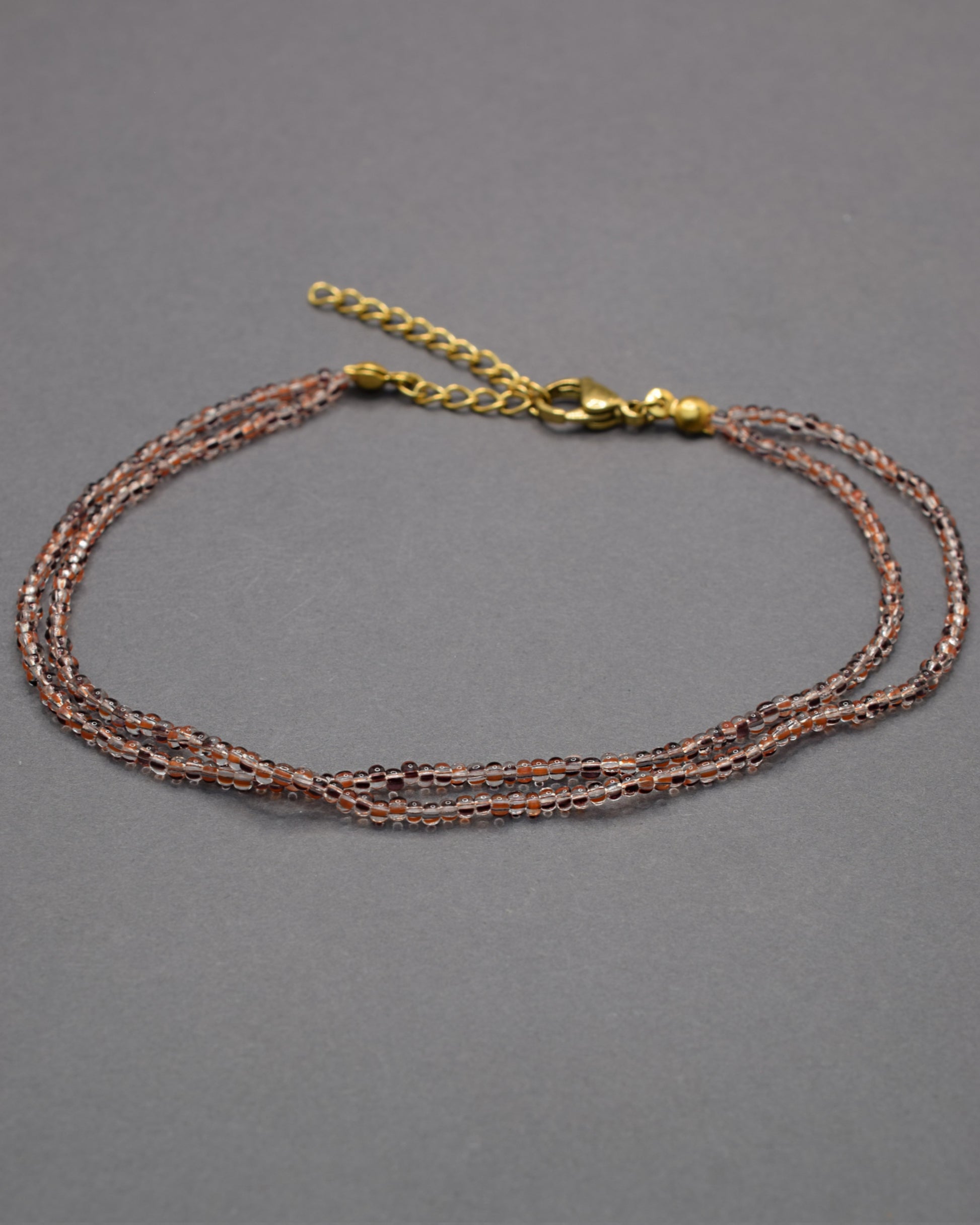 Pulseira dupla de tornozelo com missangas listradas castanhas, elegante e versátil, ideal para um toque natural e sofisticado.