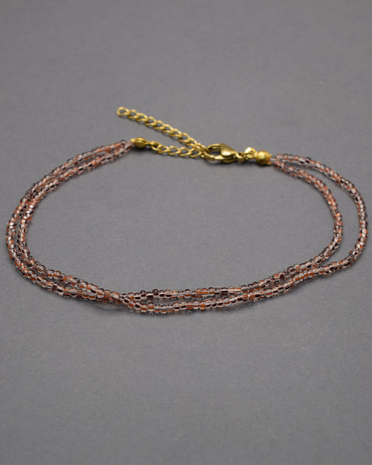 Pulseira dupla de tornozelo com missangas listradas castanhas, elegante e versátil, ideal para um toque natural e sofisticado.