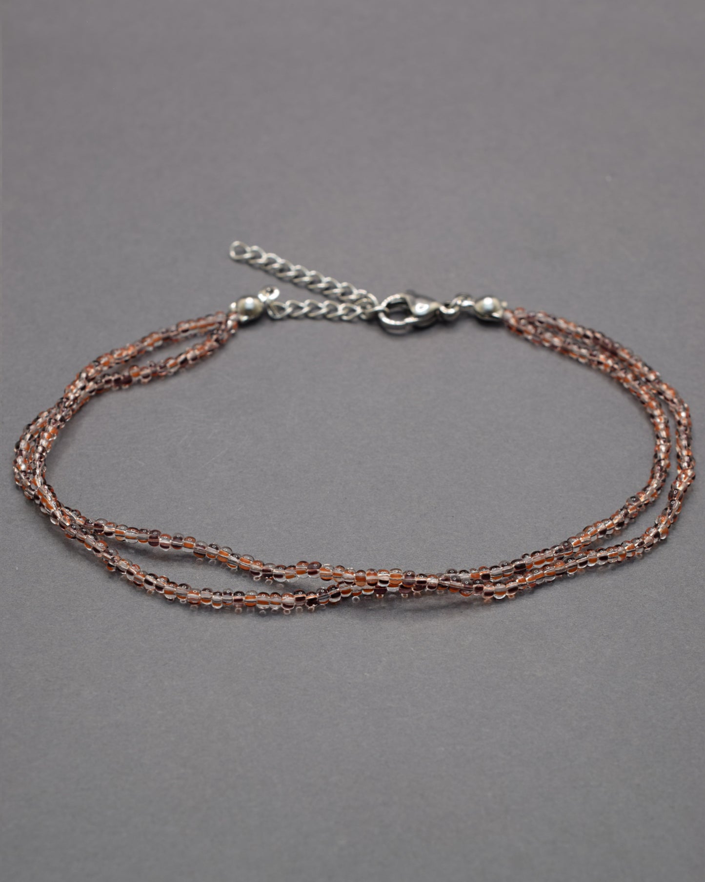 Pulseira dupla de tornozelo com missangas listradas castanhas, elegante e versátil, ideal para um toque natural e sofisticado.