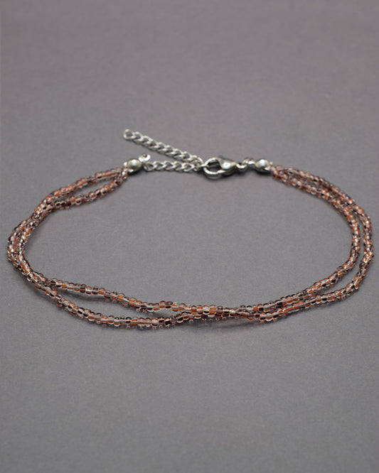 Pulseira dupla de tornozelo com missangas listradas castanhas, elegante e versátil, ideal para um toque natural e sofisticado.