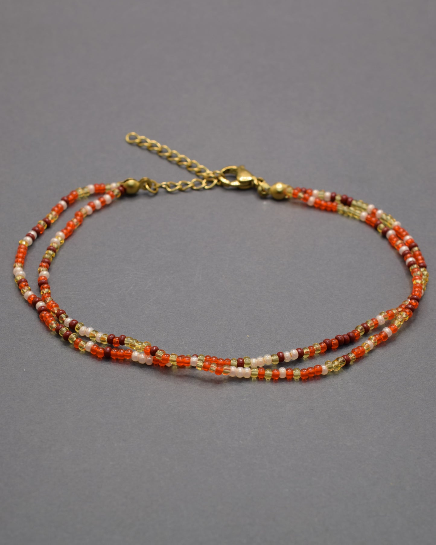 Pulseira dupla de tornozelo com missangas em tons vermelho-alaranjados, leve, vibrante e perfeita para destacar o teu estilo nos dias de verão.