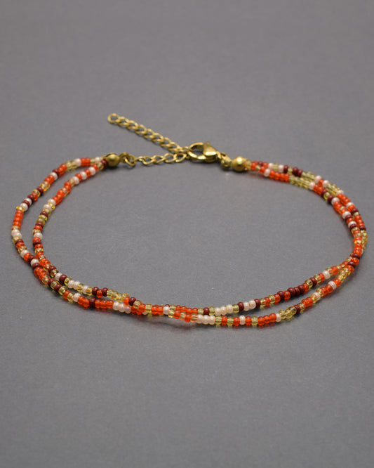 Pulseira dupla de tornozelo com missangas em tons vermelho-alaranjados, leve, vibrante e perfeita para destacar o teu estilo nos dias de verão.