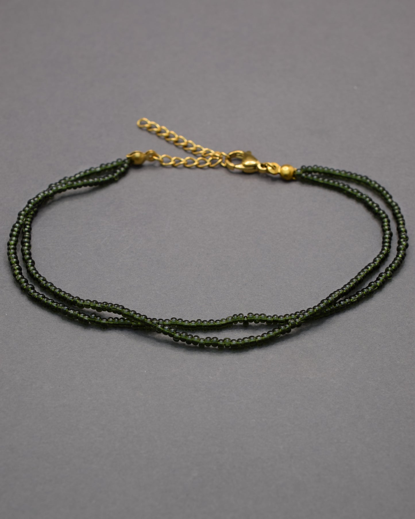 Pulseira dupla de tornozelo com missangas verde-escuras semitransparentes, elegante e envolvente, ideal para um toque natural e sofisticado.