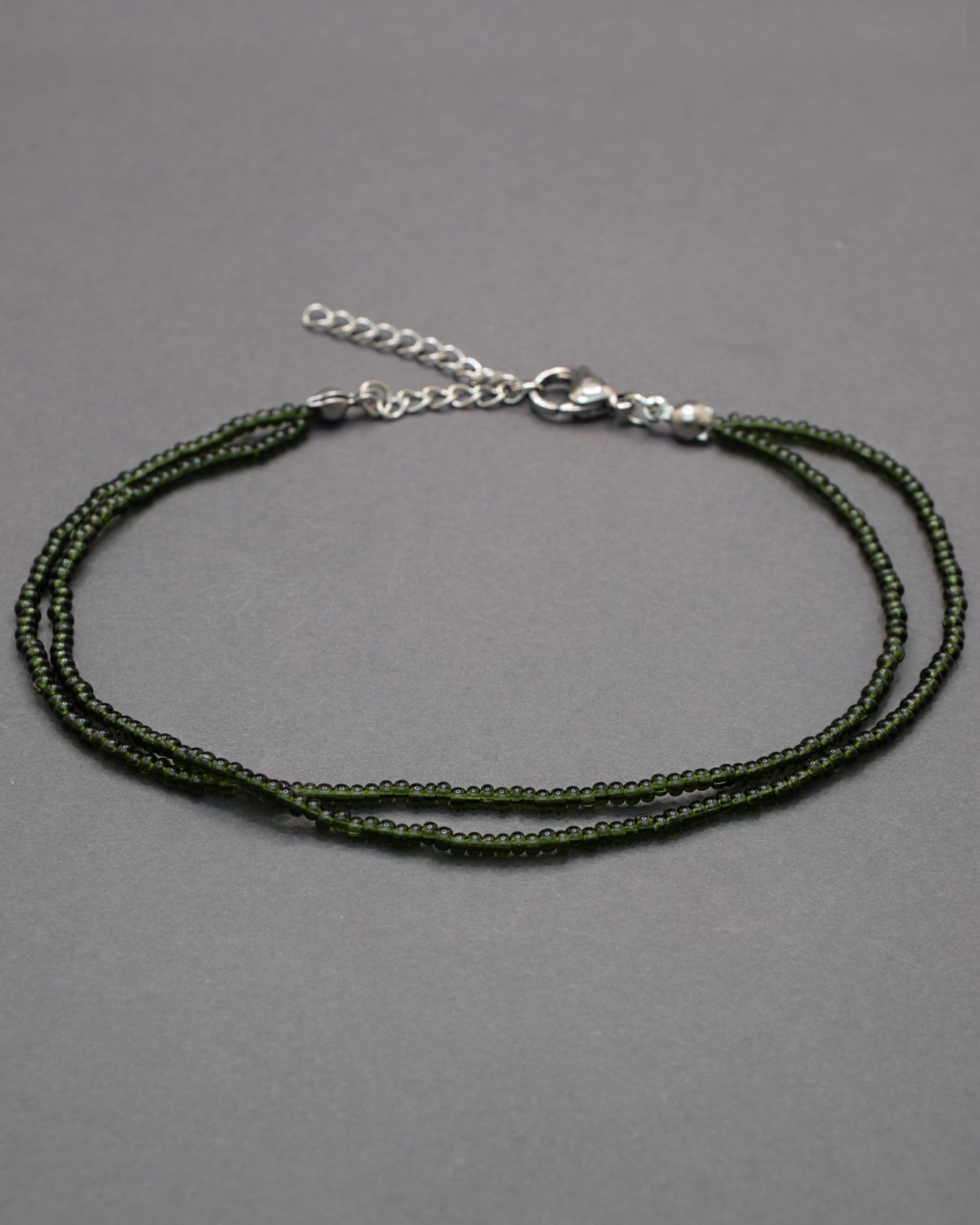 Pulseira dupla de tornozelo com missangas verde-escuras semitransparentes, elegante e envolvente, ideal para um toque natural e sofisticado.