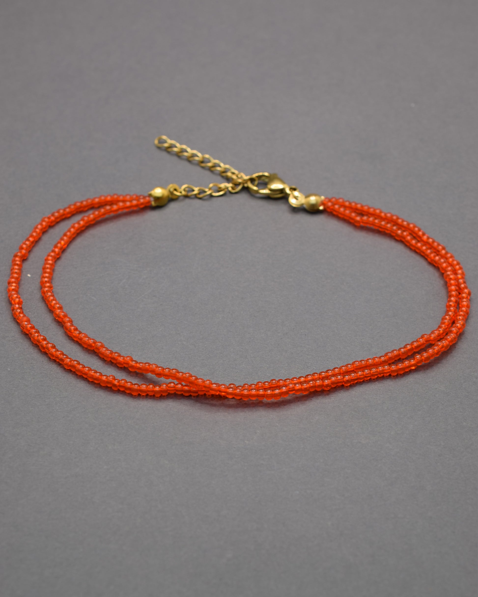 Pulseira dupla de tornozelo com missangas vermelhas-alaranjadas semitransparentes, vibrante e luminosa, perfeita para destacar o teu estilo.