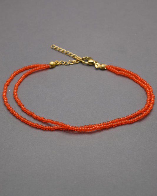 Pulseira dupla de tornozelo com missangas vermelhas-alaranjadas semitransparentes, vibrante e luminosa, perfeita para destacar o teu estilo.
