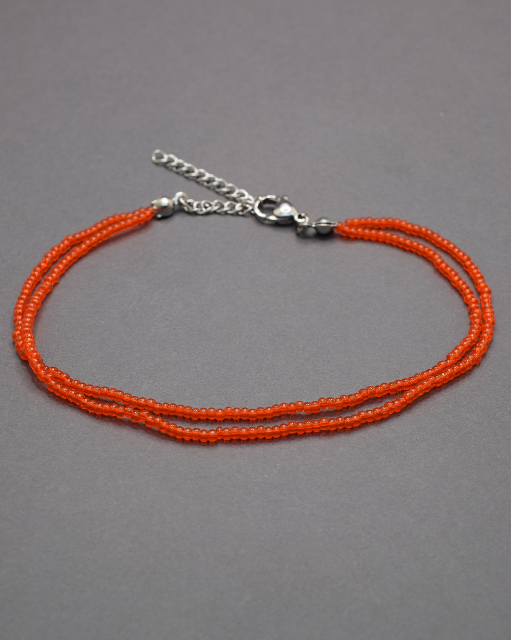 Pulseira dupla de tornozelo com missangas vermelhas-alaranjadas semitransparentes, vibrante e luminosa, perfeita para destacar o teu estilo.