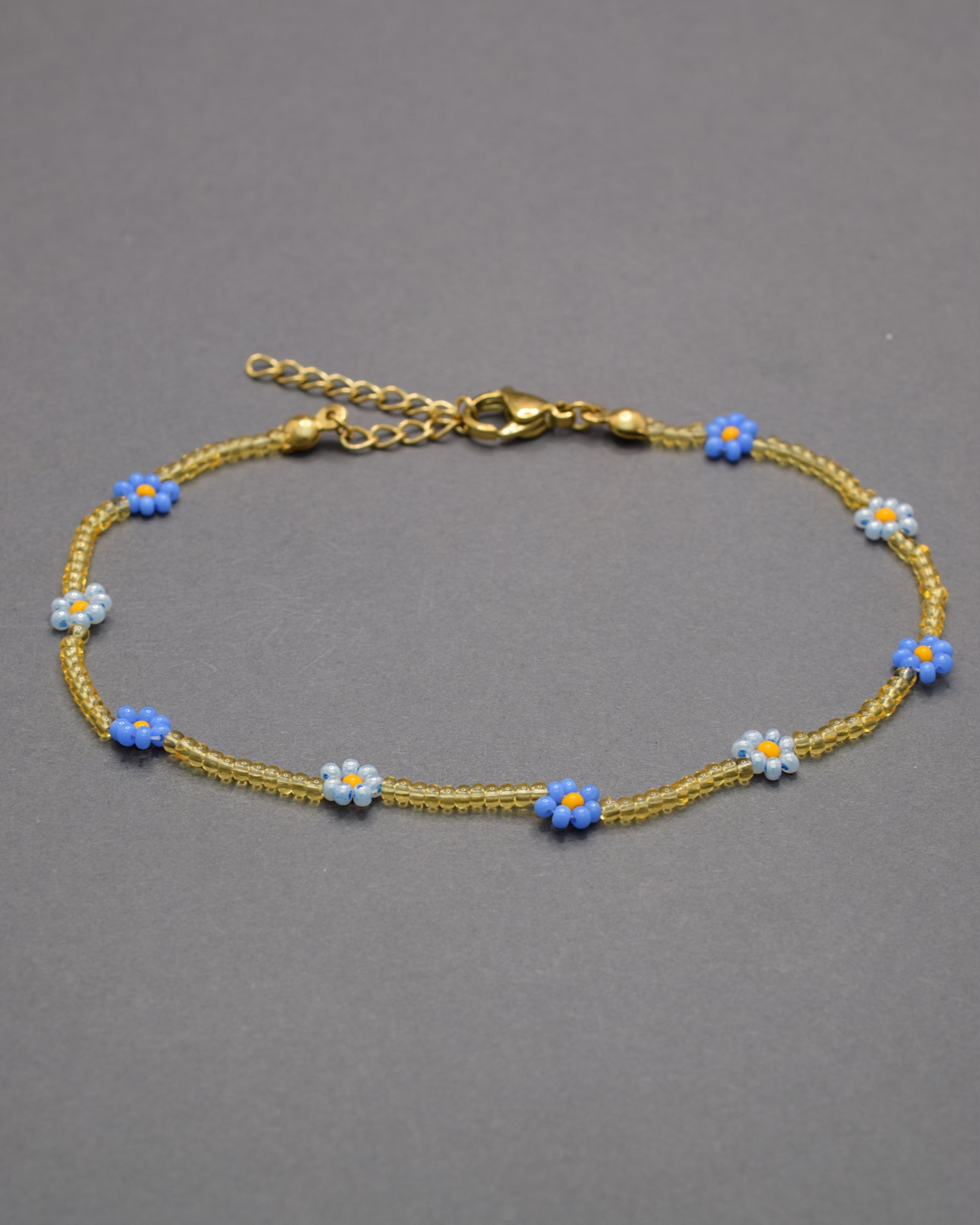 Pulseira de tornozelo com flores azul-claro e néon e missangas douradas semitransparentes, delicada e vibrante, perfeita para um look fresco.