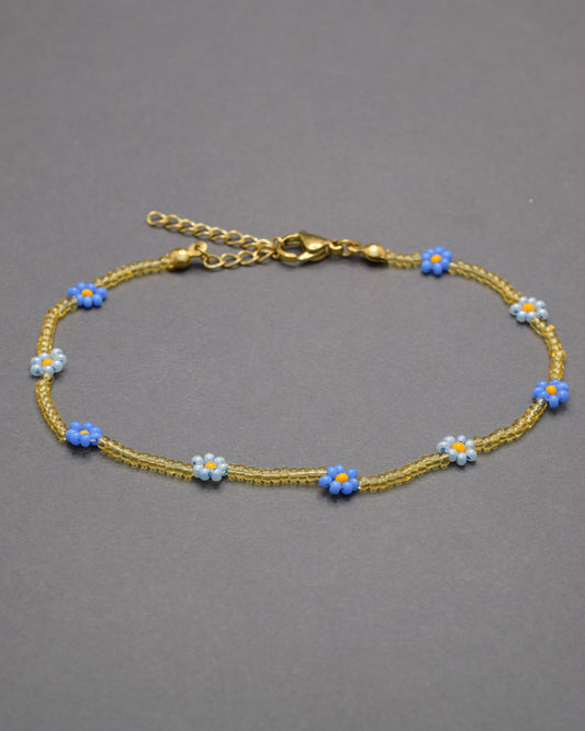Pulseira de tornozelo com flores azul-claro e néon e missangas douradas semitransparentes, delicada e vibrante, perfeita para um look fresco.