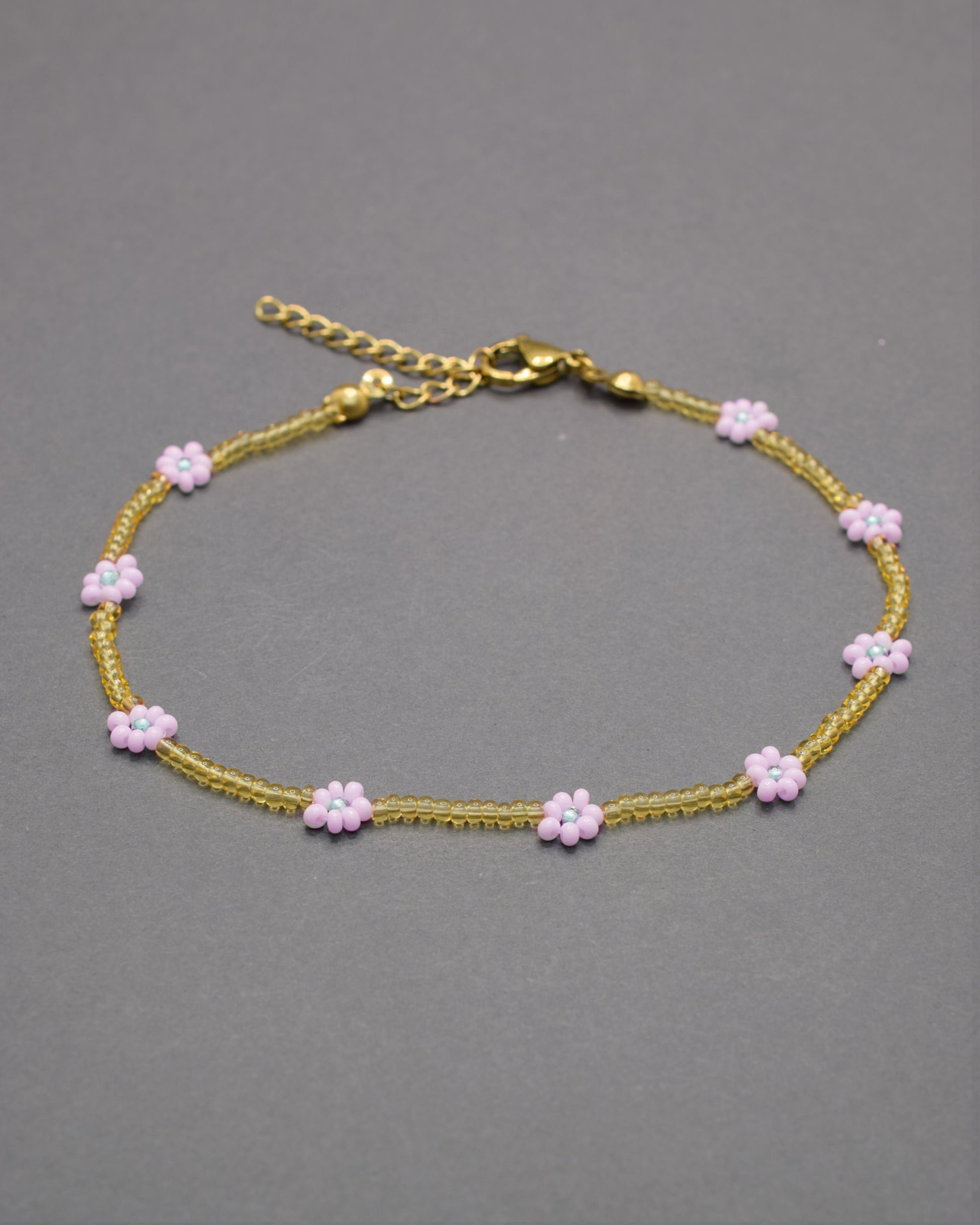 Pulseira de tornozelo com flores rosa-claro e missangas douradas semitransparentes, delicada e elegante, perfeita para um toque romântico.