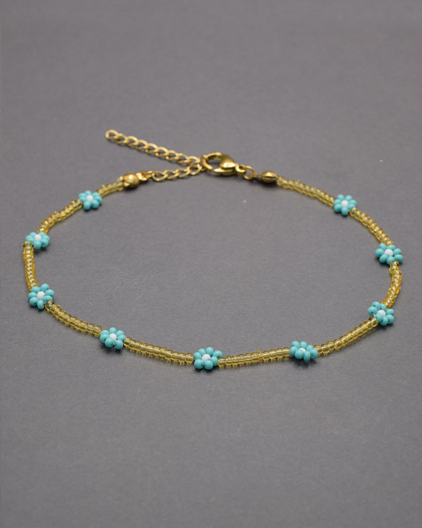 Pulseira de tornozelo com flores turquesa e missangas douradas semitransparentes, leve e vibrante, perfeita para um estilo fresco e luminoso.