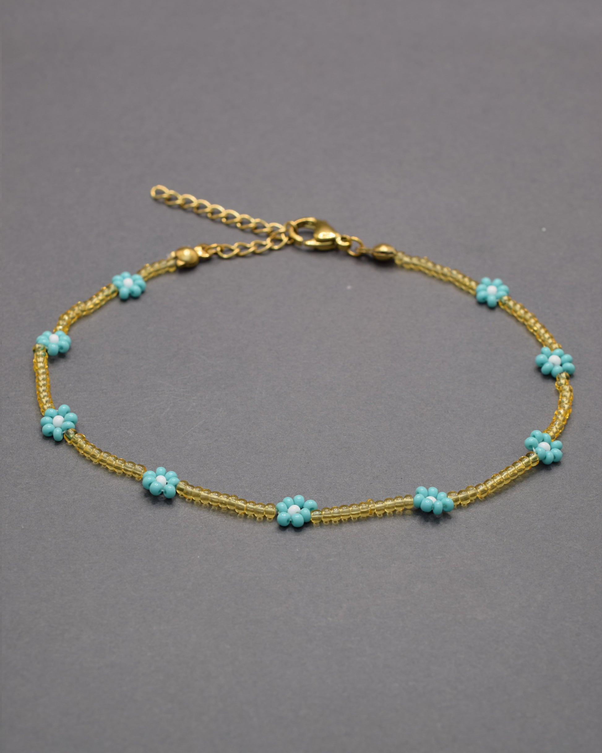 Pulseira de tornozelo com flores turquesa e missangas douradas semitransparentes, leve e vibrante, perfeita para um estilo fresco e luminoso.