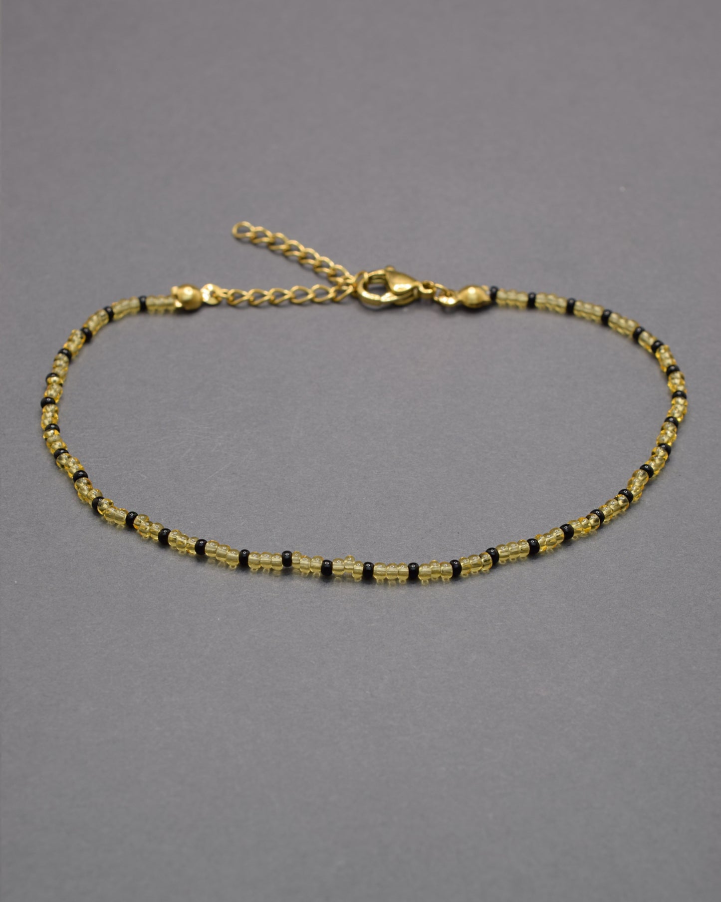 Pulseira de tornozelo com missangas douradas semitransparentes e padrão preto, elegante e moderna, perfeita para destacar o teu estilo.