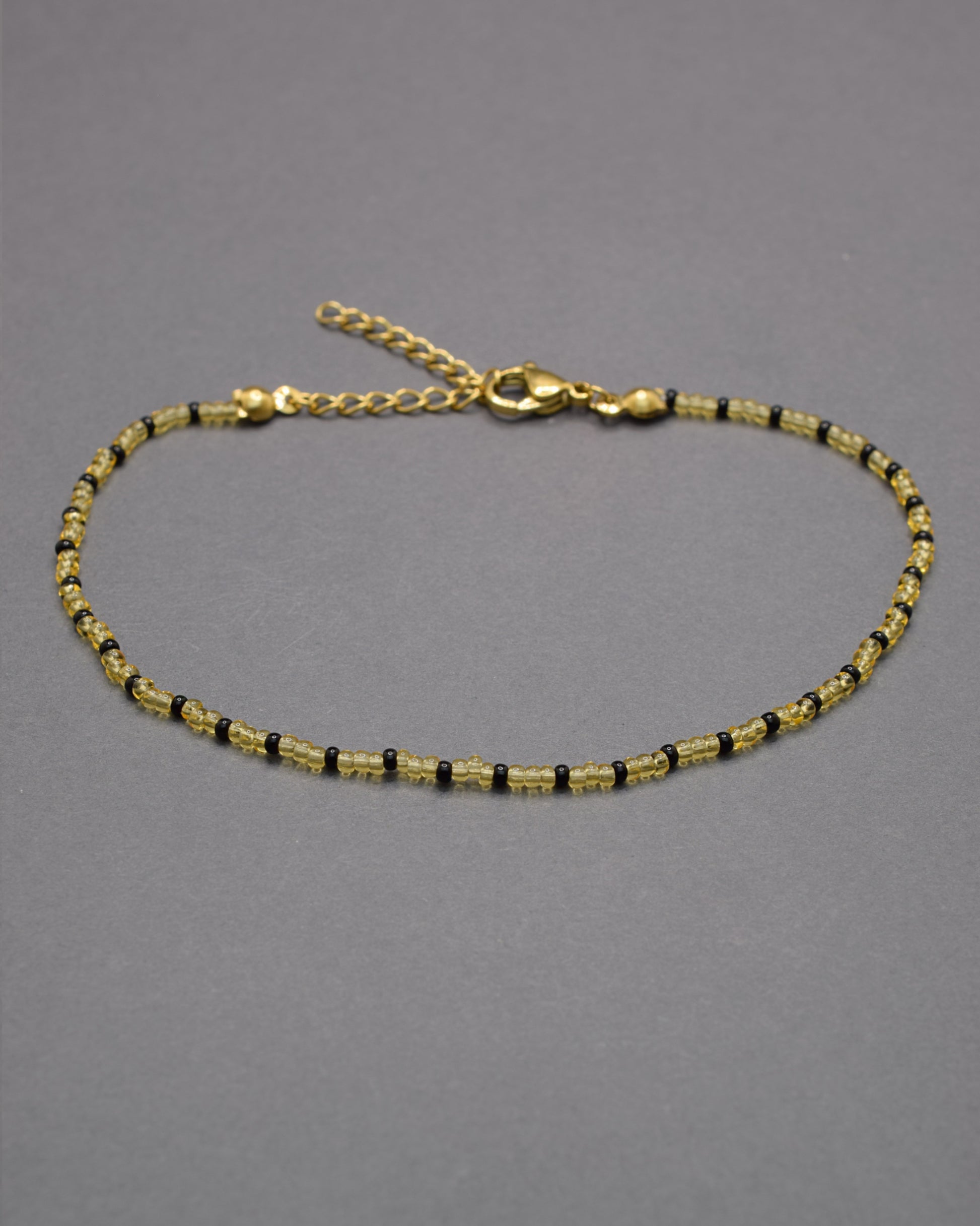 Pulseira de tornozelo com missangas douradas semitransparentes e padrão preto, elegante e moderna, perfeita para destacar o teu estilo.