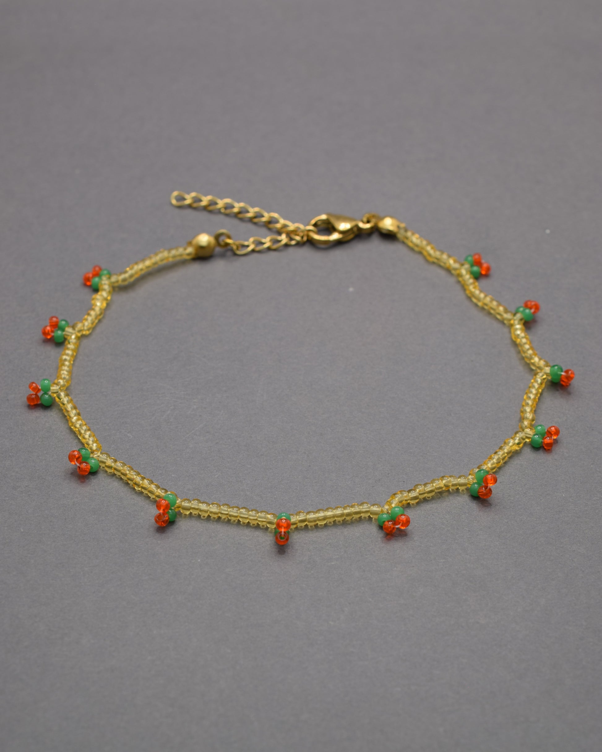 Pulseira de tornozelo com cerejas em missangas douradas semitransparentes, delicada e divertida, perfeita para um toque doce e brilhante.