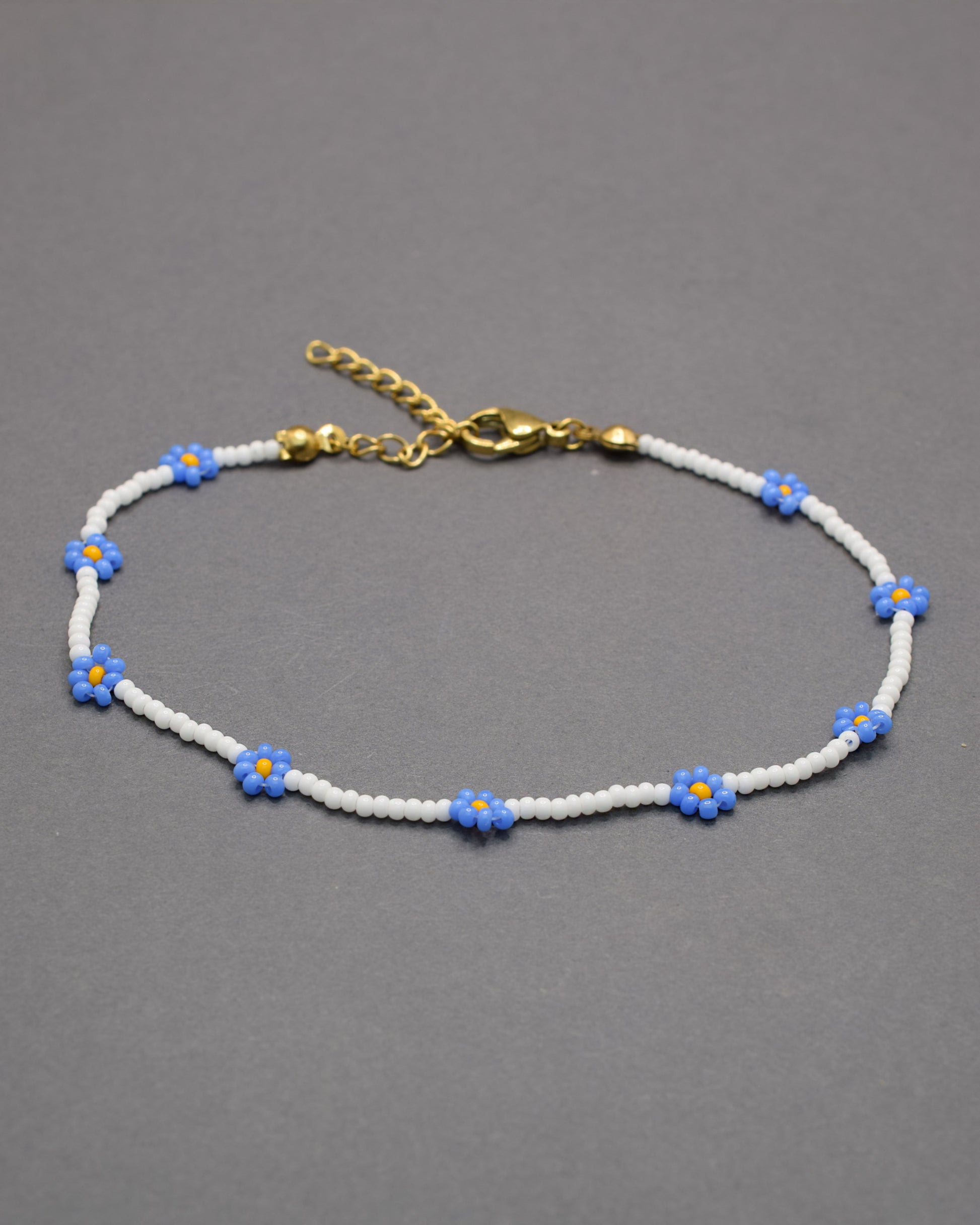 Pulseira de tornozelo em missangas brancas com flores azuis. Delicada e leve, perfeita para um toque fresco e elegante no dia a dia.