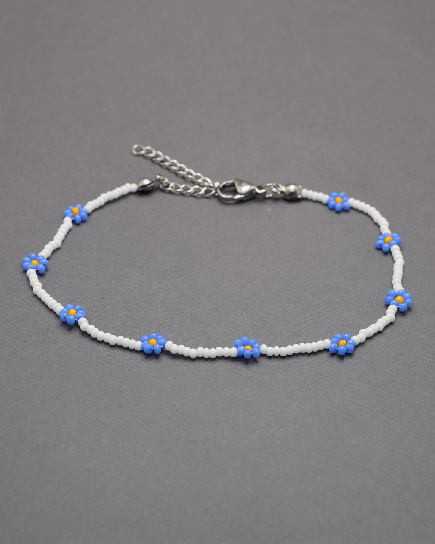 Pulseira de tornozelo em missangas brancas com flores azuis. Delicada e leve, perfeita para um toque fresco e elegante no dia a dia.