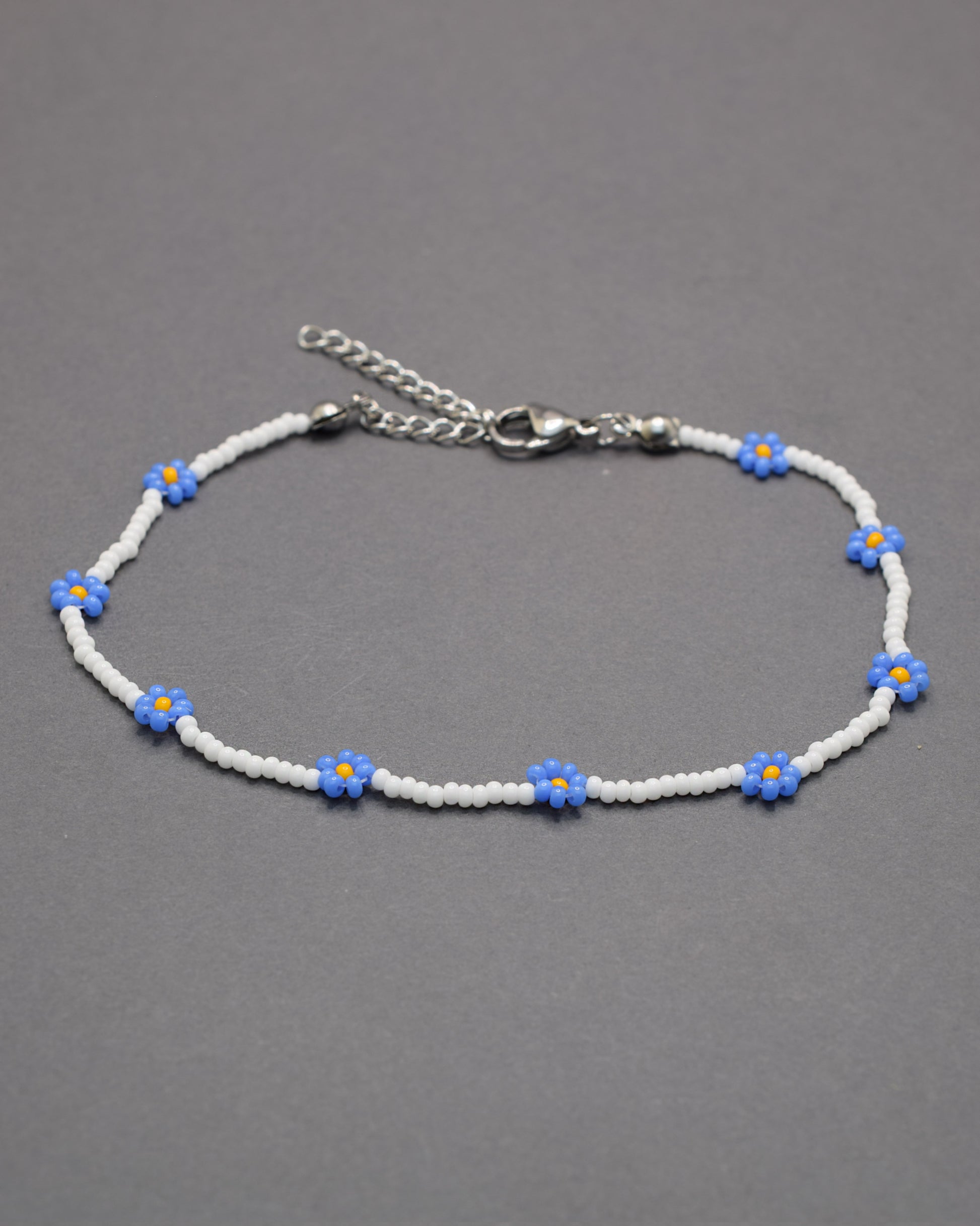 Pulseira de tornozelo em missangas brancas com flores azuis. Delicada e leve, perfeita para um toque fresco e elegante no dia a dia.