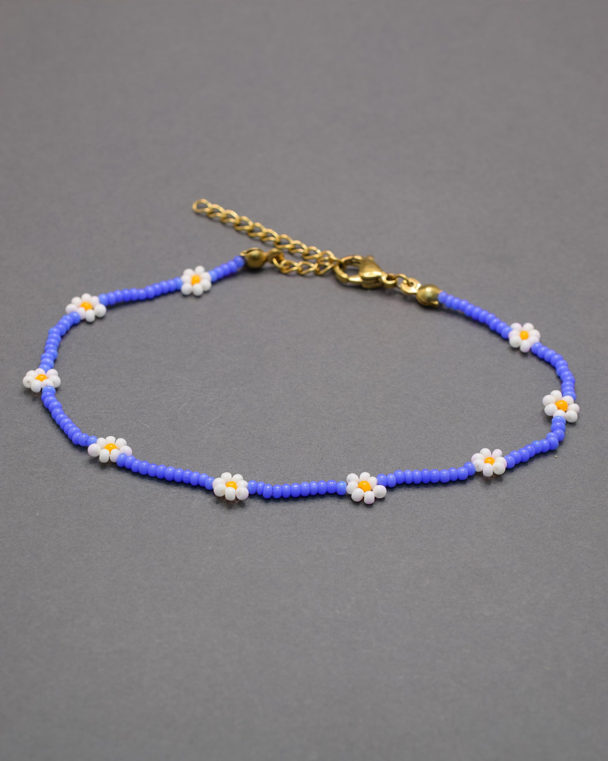 Pulseira de tornozelo em missangas azul néon com flores brancas. Leve, vibrante e perfeita para dar um toque divertido e moderno ao teu look.
