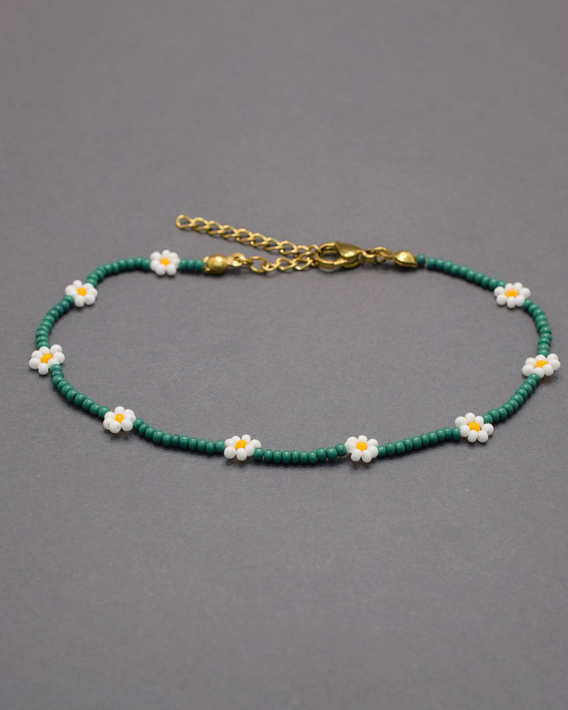 Pulseira de tornozelo em missangas verdes com flores brancas. Leve e fresca, ideal para um toque natural e delicado no teu estilo.