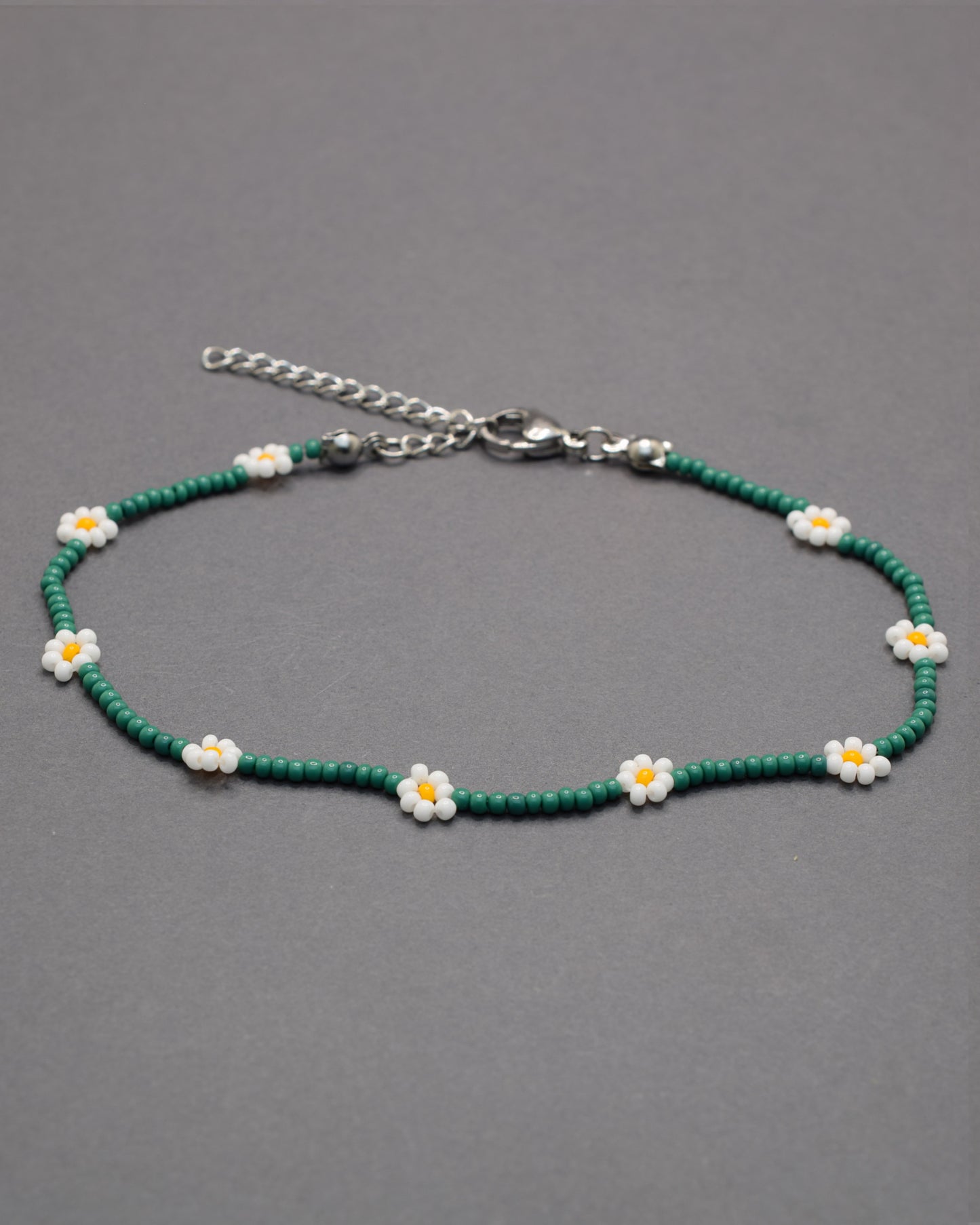 Pulseira de tornozelo em missangas verdes com flores brancas. Leve e fresca, ideal para um toque natural e delicado no teu estilo.