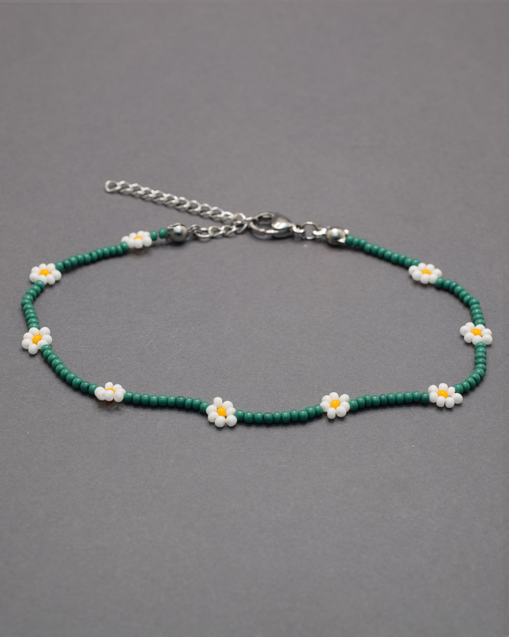 Pulseira de tornozelo em missangas verdes com flores brancas. Leve e fresca, ideal para um toque natural e delicado no teu estilo.