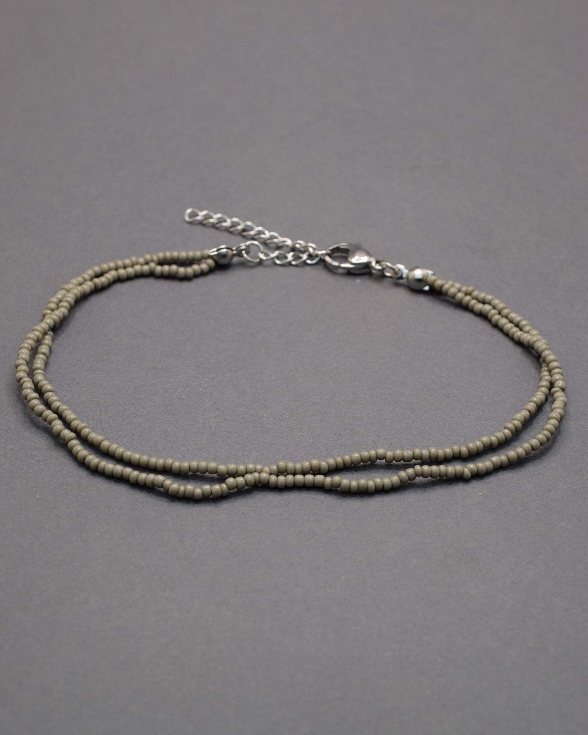Pulseira dupla de tornozelo com missangas cinzentas. Elegante, discreta e perfeita para complementar qualquer look com estilo moderno.