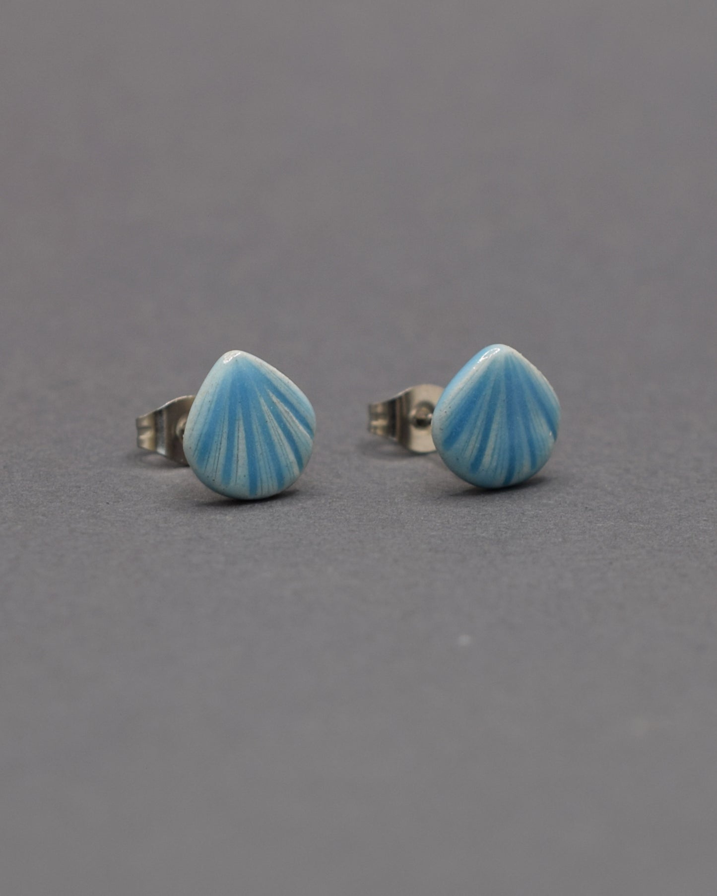 Brincos stud de cerâmica com delicado design de concha em azul claro. Leves, elegantes e ideais para um toque de charme ao seu look.