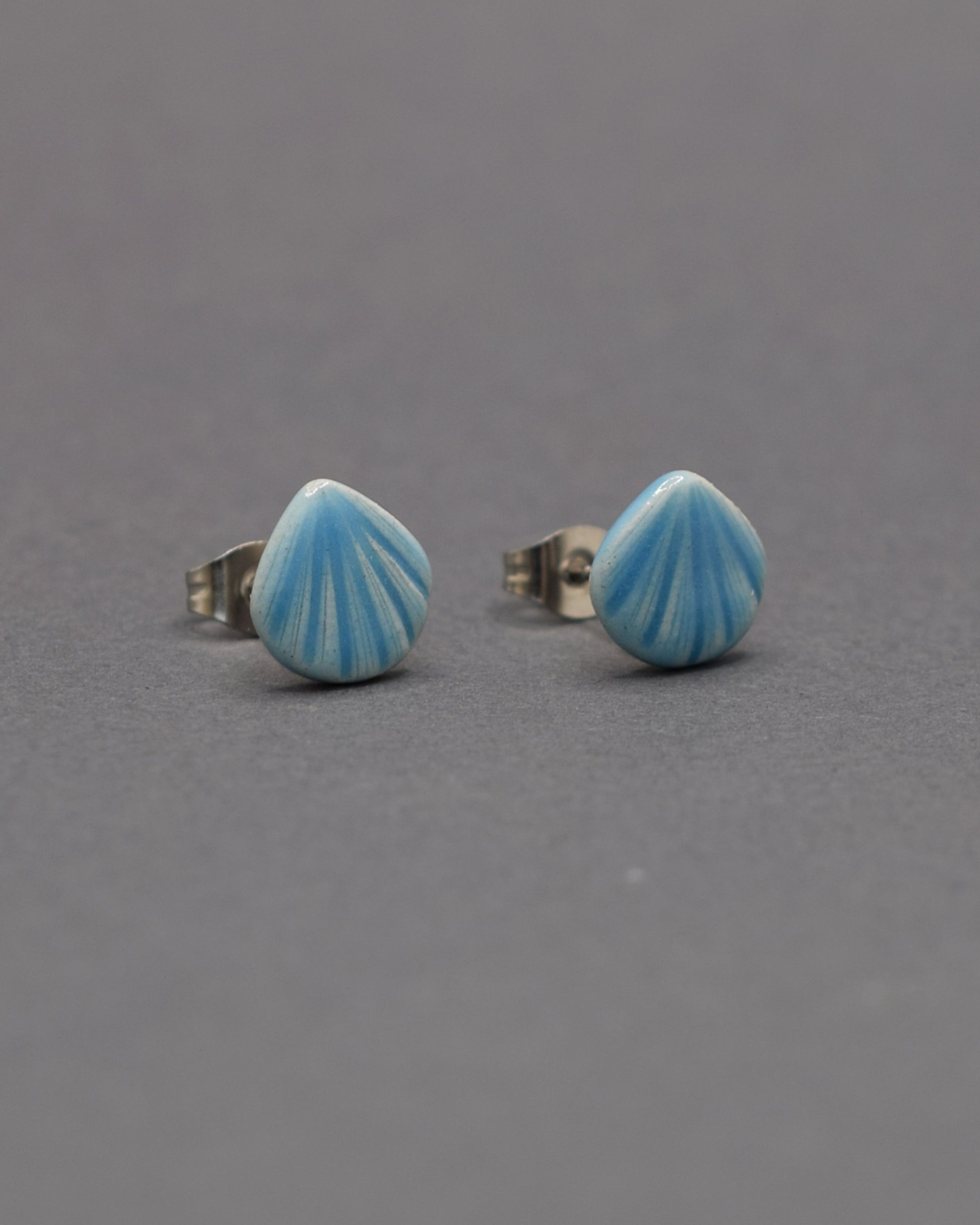 Brincos stud de cerâmica com delicado design de concha em azul claro. Leves, elegantes e ideais para um toque de charme ao seu look.
