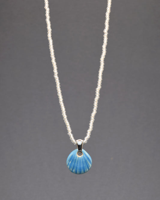 Encante-se com este colar de missangas de vidro brancas semitransparentes, adornado com um pendente de concha em cerâmica azul clara. Com um design delicado e artesanal, ele traz um toque de elegância serena e sofisticação ao seu visual. Perfeito para qualquer ocasião.