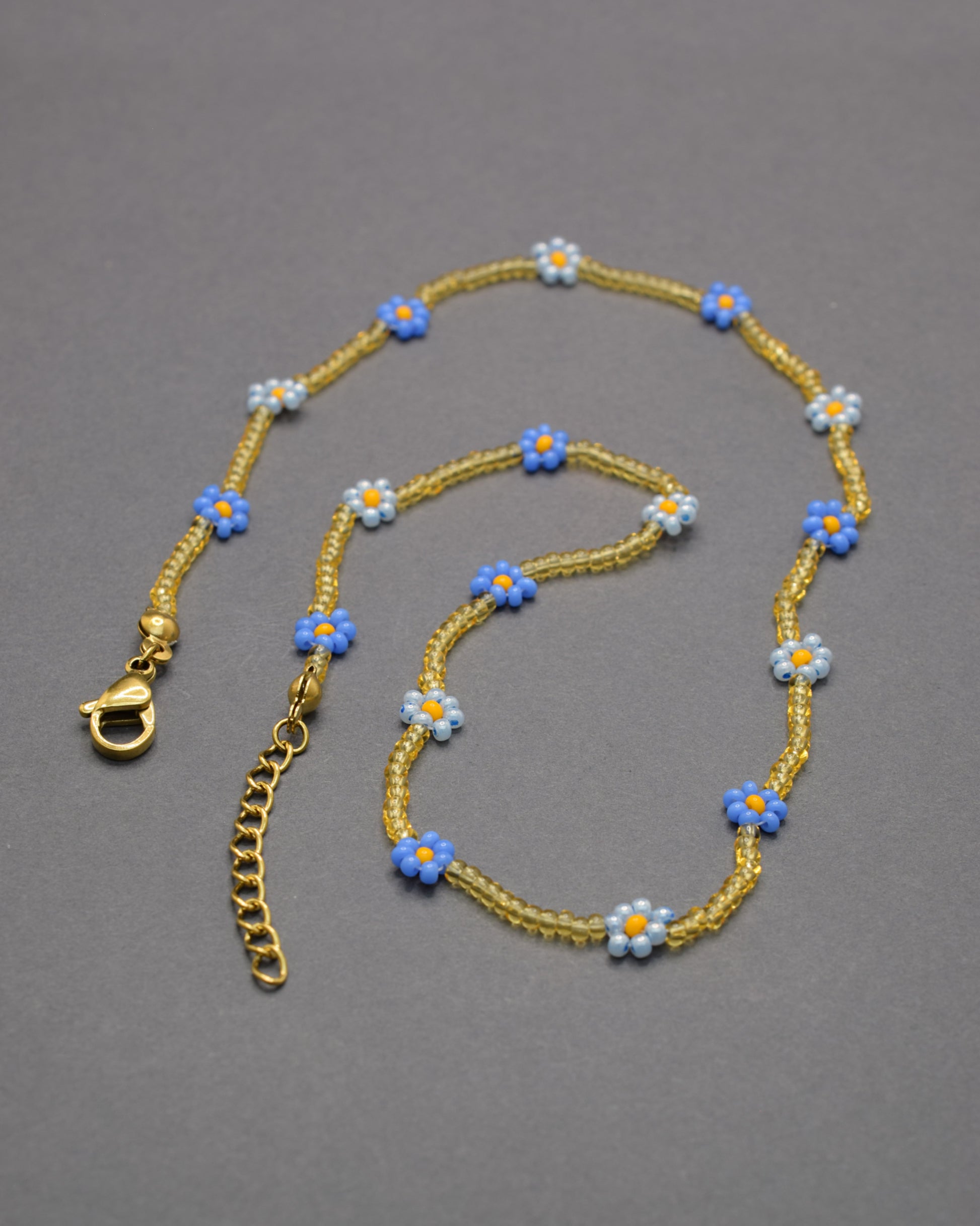 Colar com flores azul-claras e néon e missangas douradas semitransparentes, vibrante e delicado, perfeito para iluminar o teu estilo.