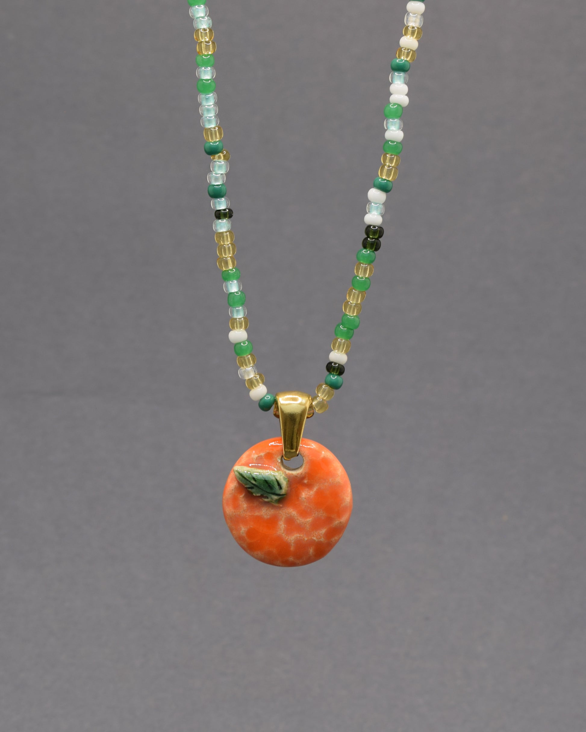 Colar com laranja e folha em cerâmica pintada à mão. Um apontamento de cor inspirado nos pomares portugueses, perfeito para dar vida a qualquer look.