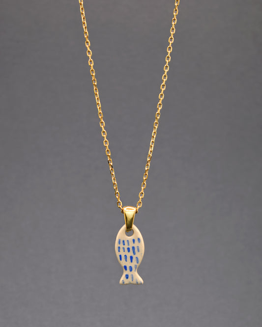 Este colar, com a sua corrente em aço inoxidável dourado, apresenta um charmoso pendente de peixe em cerâmica, pintado à mão com nuances em azul que imitam escamas. Uma fusão perfeita de elegância e arte.