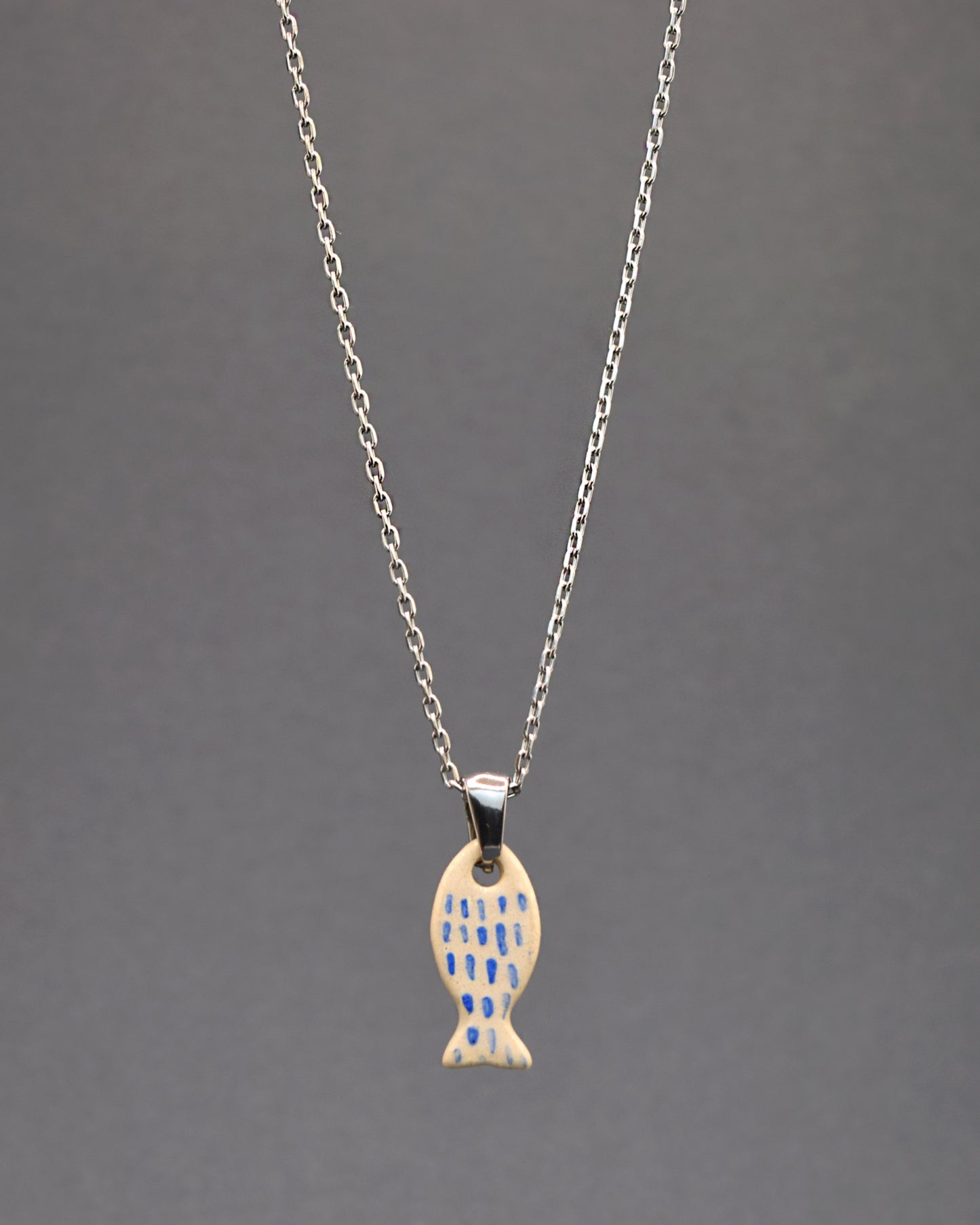  Colar em aço inoxidável com pendente de peixe em cerâmica, pintado à mão com delicadas pinceladas em azul, remetendo às escamas. Uma peça única que combina durabilidade com arte artesanal.