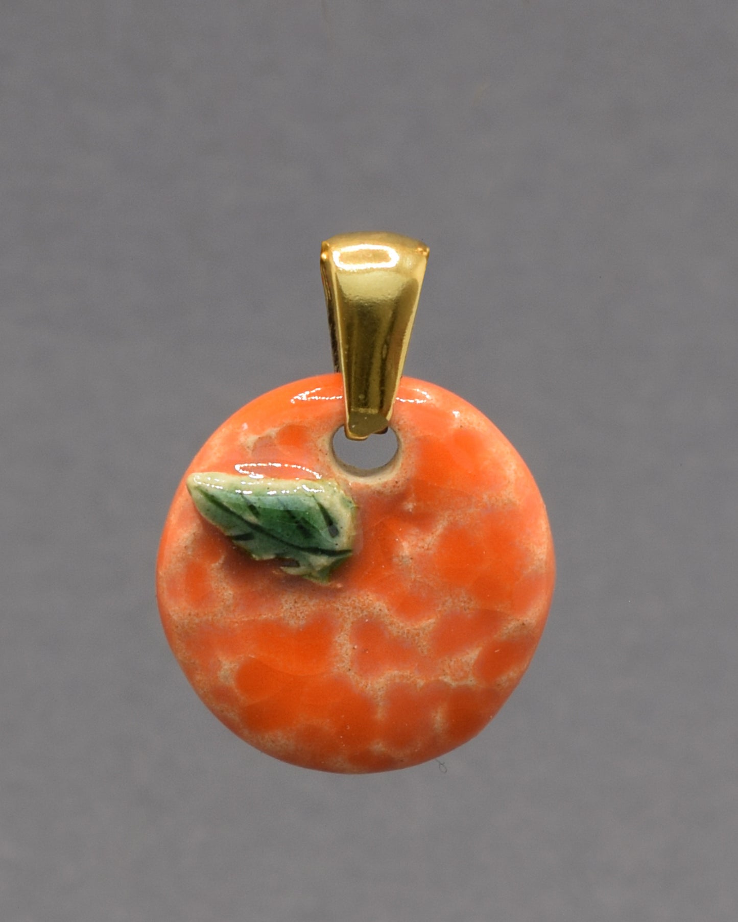 Pendente de cerâmica pintado à mão com uma laranja e a sua folha. Uma peça delicada e cheia de cor, inspirada na simplicidade e beleza dos frutos naturais.