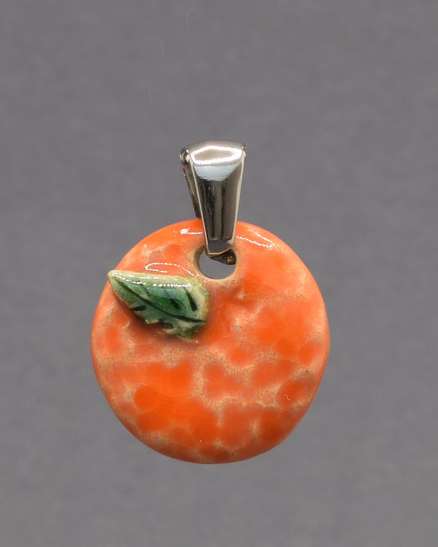 Pendente de cerâmica pintado à mão com uma laranja e a sua folha. Uma peça delicada e cheia de cor, inspirada na simplicidade e beleza dos frutos naturais.