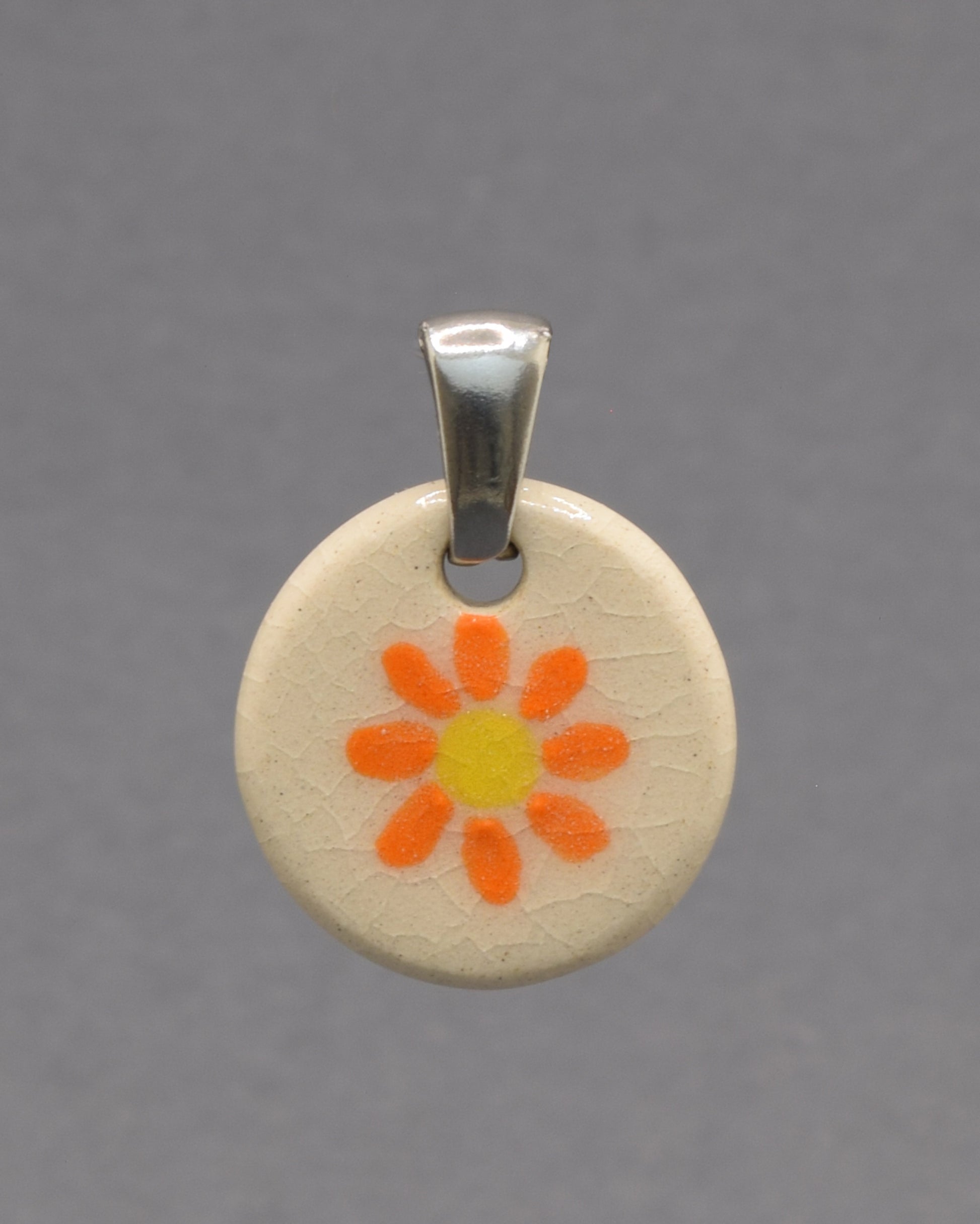 Pendente de cerâmica pintado à mão com uma delicada margarida laranja. As cores vibrantes e o acabamento artesanal tornam cada peça única e cheia de encanto.