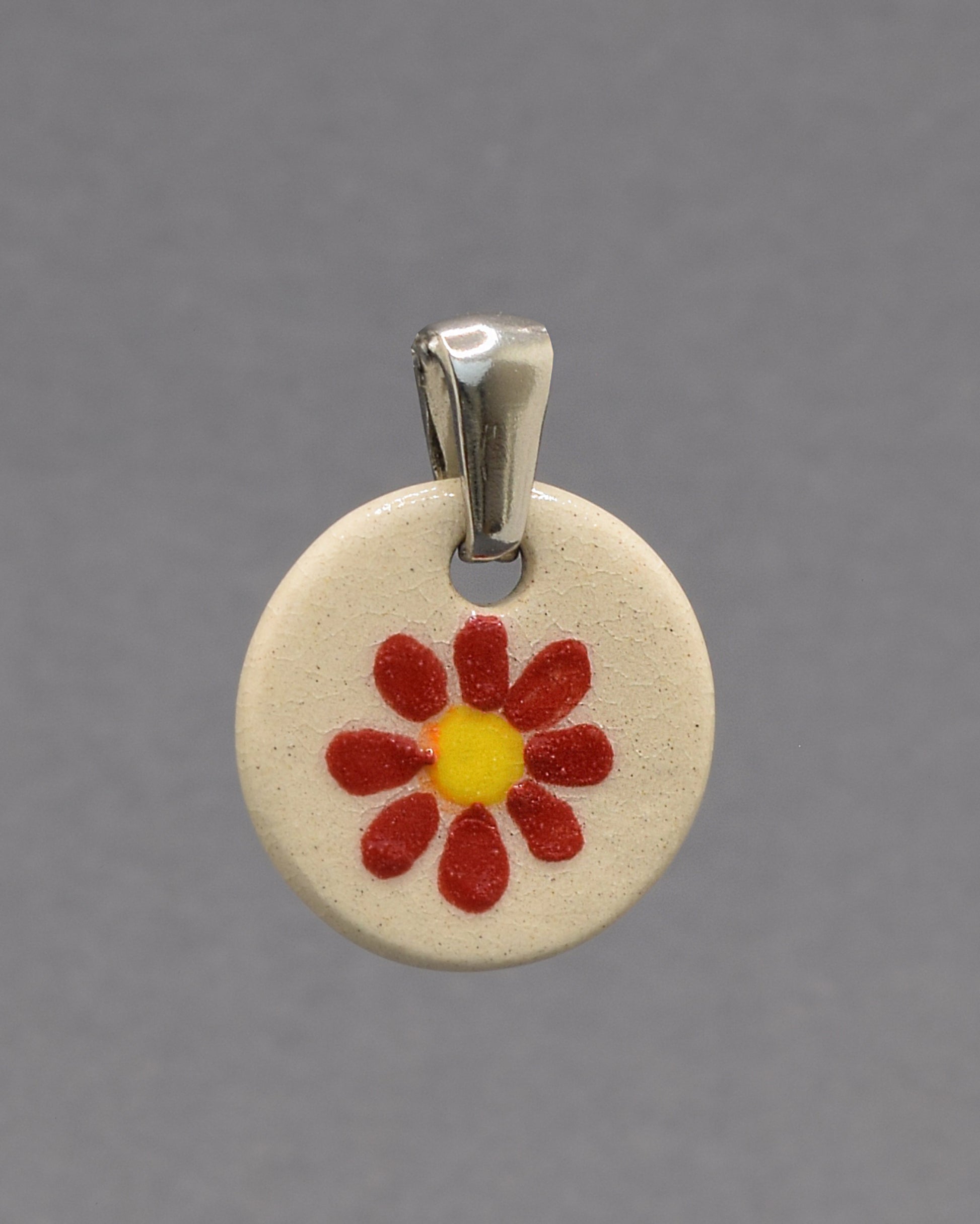 Pendente de cerâmica pintado à mão com uma delicada margarida vermelha. Uma peça artesanal que combina elegância, cor e um toque inspirado na natureza.