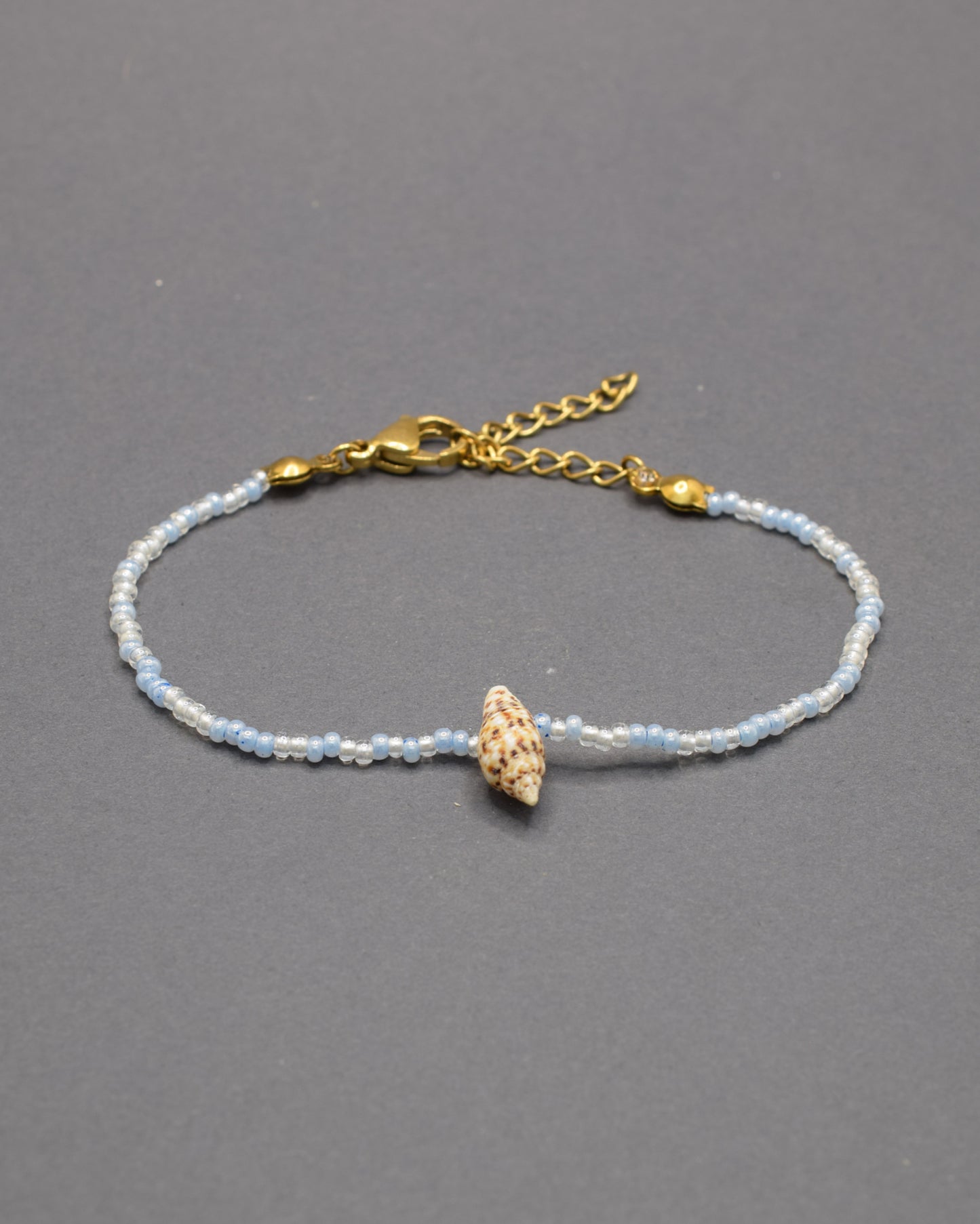Pulseira com búzio natural e missangas de vidro em tons de azul claro, delicada e luminosa, trazendo um toque fresco e autêntico ao teu estilo.