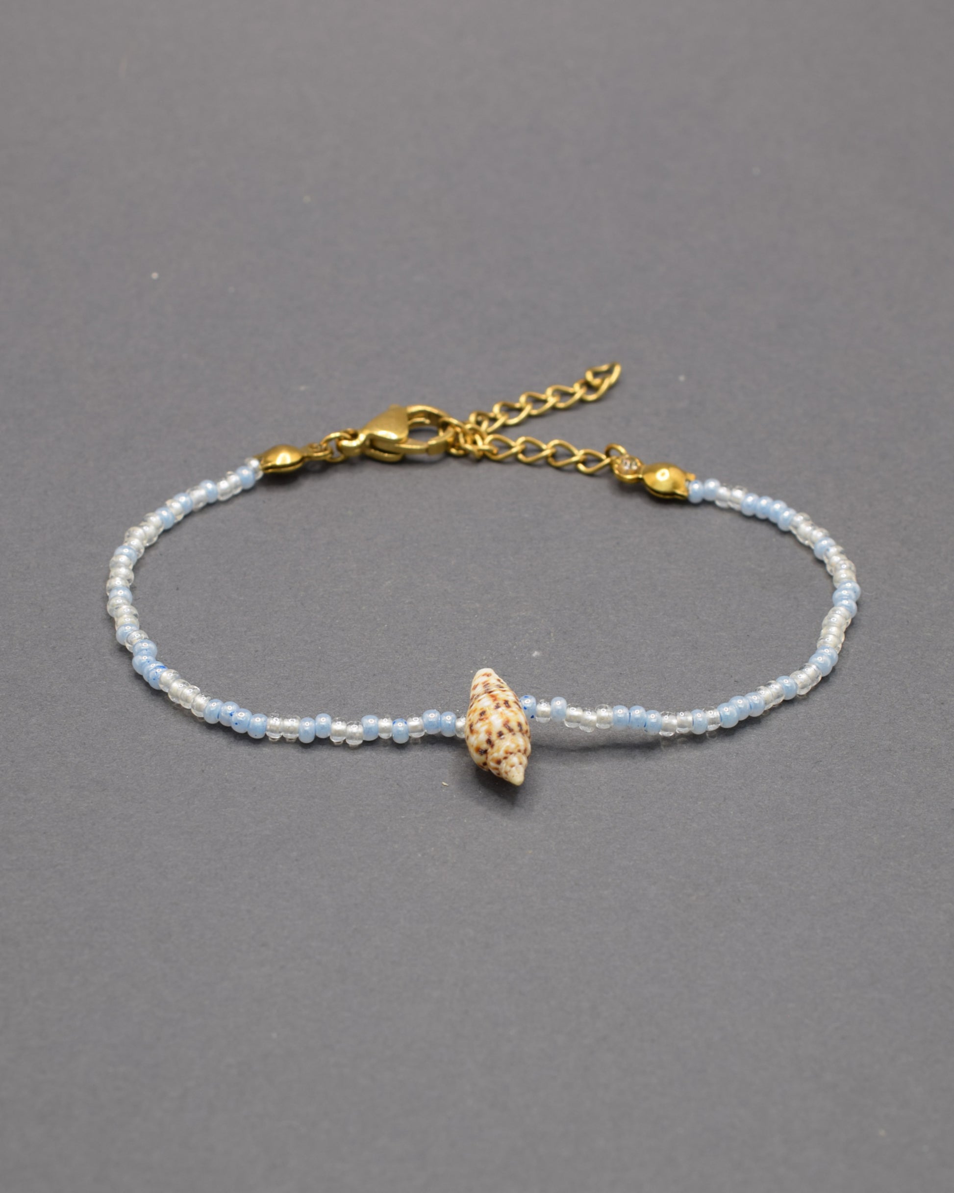 Pulseira com búzio natural e missangas de vidro em tons de azul claro, delicada e luminosa, trazendo um toque fresco e autêntico ao teu estilo.